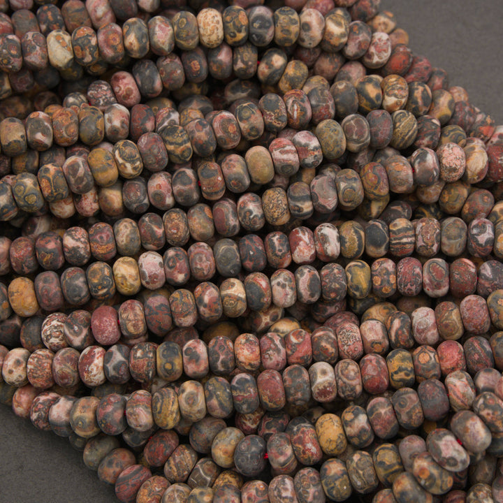 A close-up pile of small polished stone beads with a mottled marbled pattern in earthy tones of brown, gray, red, beige, and black.