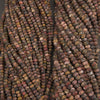 Multiple strands of round stone beads in earthy marbled colors, including brown, red, gray, black, and beige, arranged vertically.