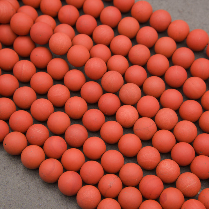 A close-up arrangement of many small matte orange-red spherical beads or balls spread across a gray surface.