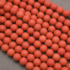 A close-up arrangement of many small matte orange-red spherical beads or balls spread across a gray surface.