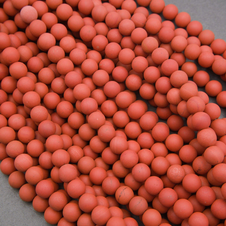 A pile of small matte orange-red spherical beads or balls filling most of the frame, with a gray surface visible in the lower-left corner.