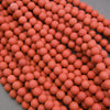 A pile of small matte orange-red spherical beads or balls filling most of the frame, with a gray surface visible in the lower-left corner.