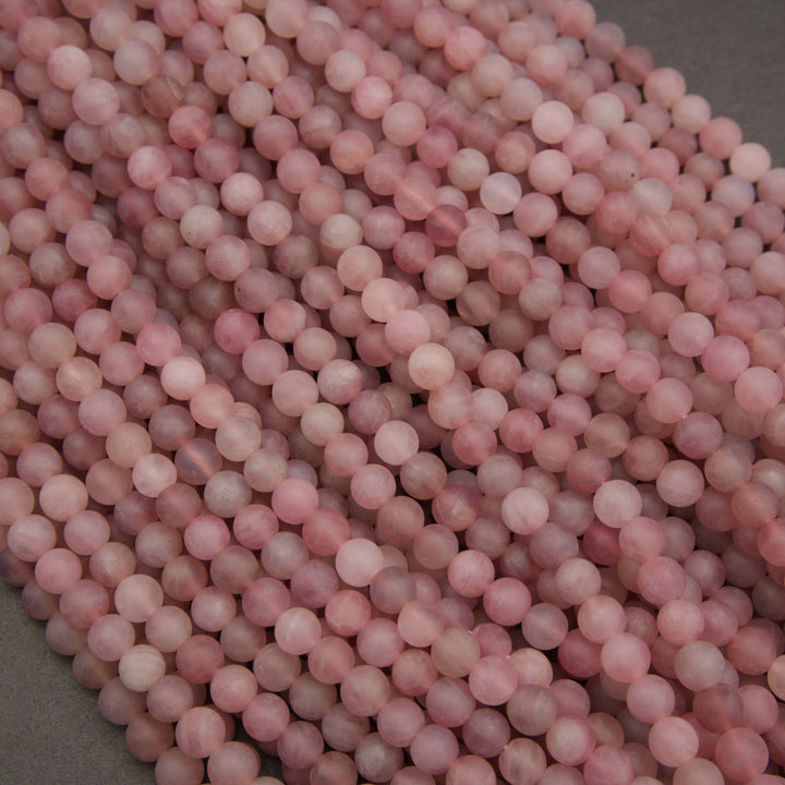 A close-up pile of round, pale pink beads with subtle white marbling, filling almost the entire frame against a dark gray background.
