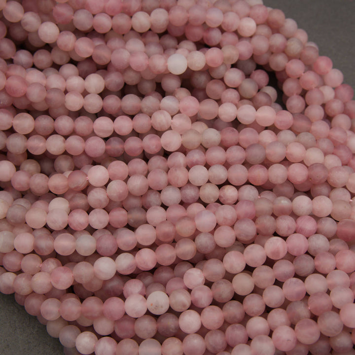 A close-up of many small round pink beads strung together in long strands, filling most of the frame against a dark gray background.
