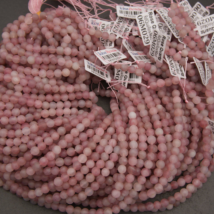 A pile of pink rose quartz gemstone beads with white identification tags attached, photographed on a neutral gray surface.