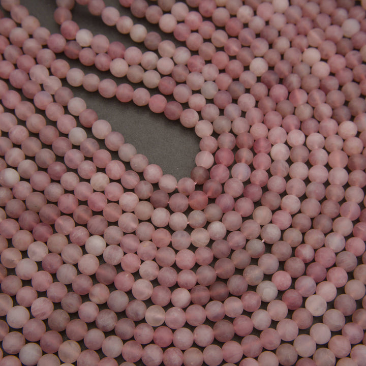 Close-up of multiple strands of round, matte pink beads arranged on a dark gray surface.