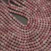 Close-up of multiple strands of round, matte pink beads arranged on a dark gray surface.