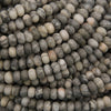 A close-up pile of small oval stone beads in mixed gray, white, beige, and black marbled patterns.