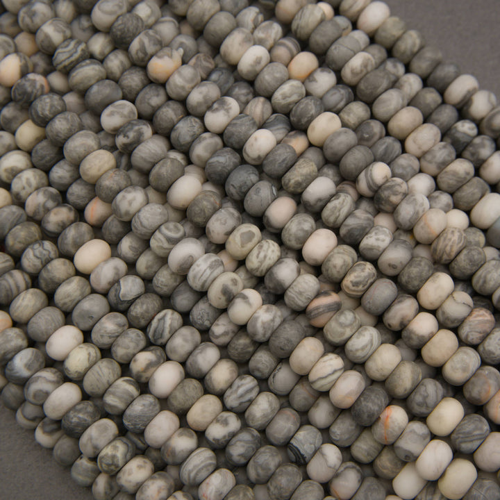 A close-up pile of small oval beads with a marbled stone pattern in shades of gray, beige, and white.