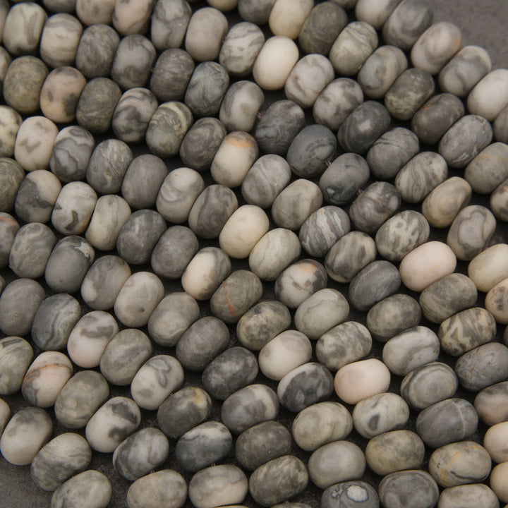 A close-up pile of smooth, rounded pebble-shaped beads in natural stone colors, featuring marbled patterns of gray, beige, white, and brown.