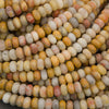 A close-up pile of small oval beads made from marbled stone, showing natural variations in color including cream, yellow, orange, pink, and gray.