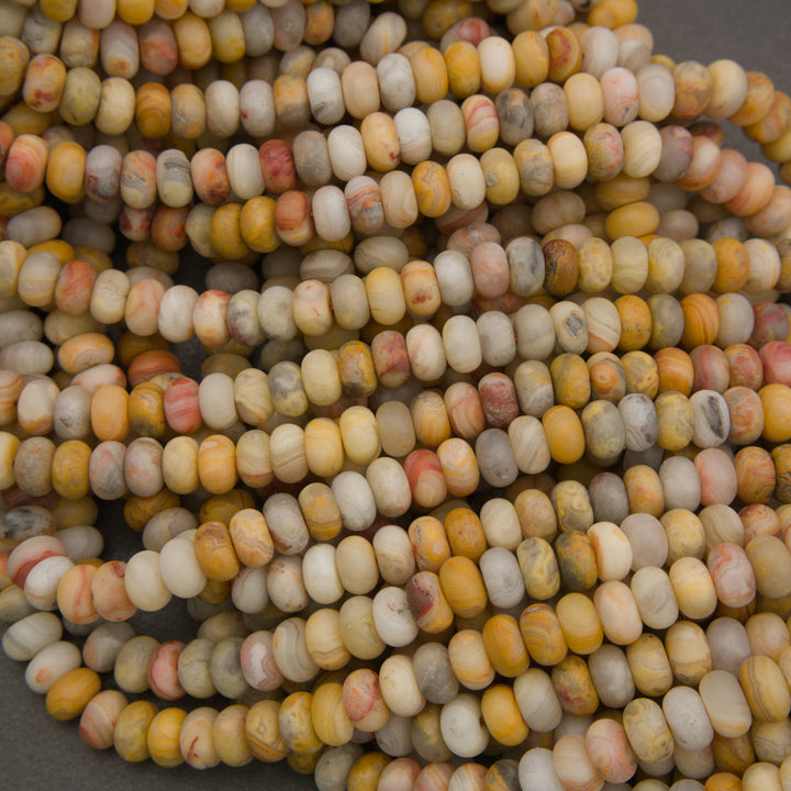 A close-up pile of small cylindrical beads made from a marbled stone with natural variations in yellow, beige, white, gray, and muted orange.