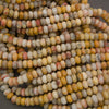 A close-up pile of small cylindrical beads made from a marbled stone with natural variations in yellow, beige, white, gray, and muted orange.