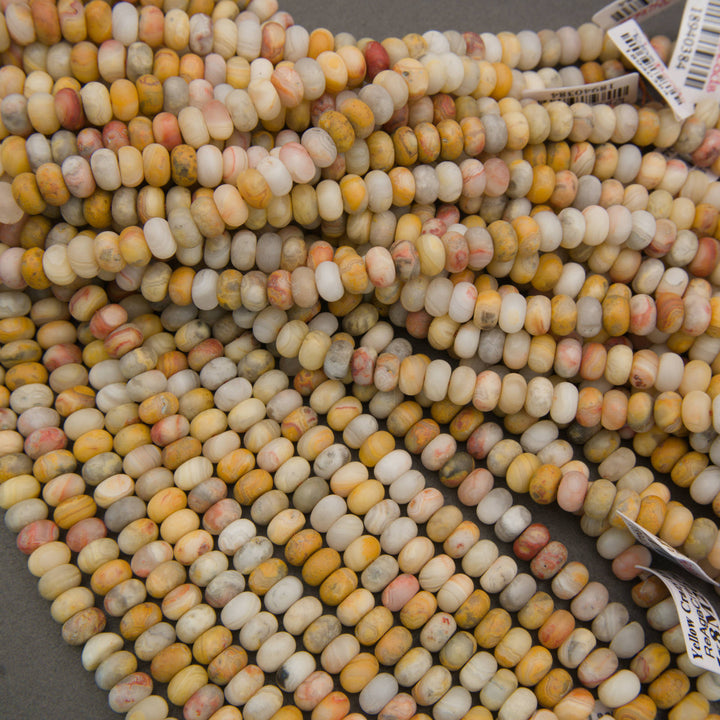 Multiple strands of small cylindrical beads in a marbled mix of cream, yellow, orange, pink, and gray tones, with some product tags visible.