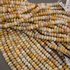 Multiple strands of small cylindrical beads in a marbled mix of cream, yellow, orange, pink, and gray tones, with some product tags visible.