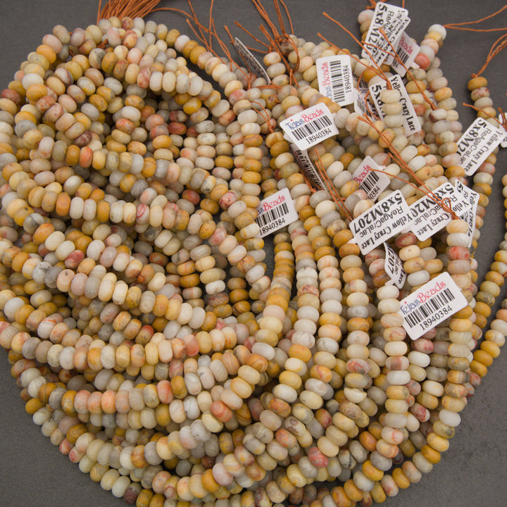 Multiple strands of small cylindrical beads in a marbled mix of cream, yellow, orange, pink, and gray tones, with some product tags visible.