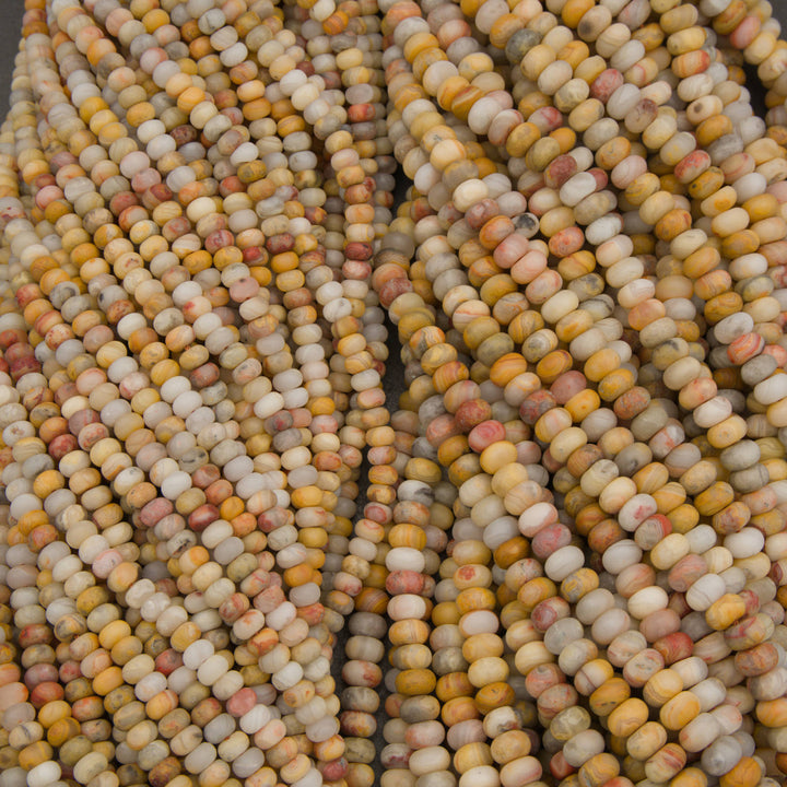 Multiple strands of small cylindrical beads in a marbled mix of cream, yellow, orange, pink, and gray tones, with some product tags visible.