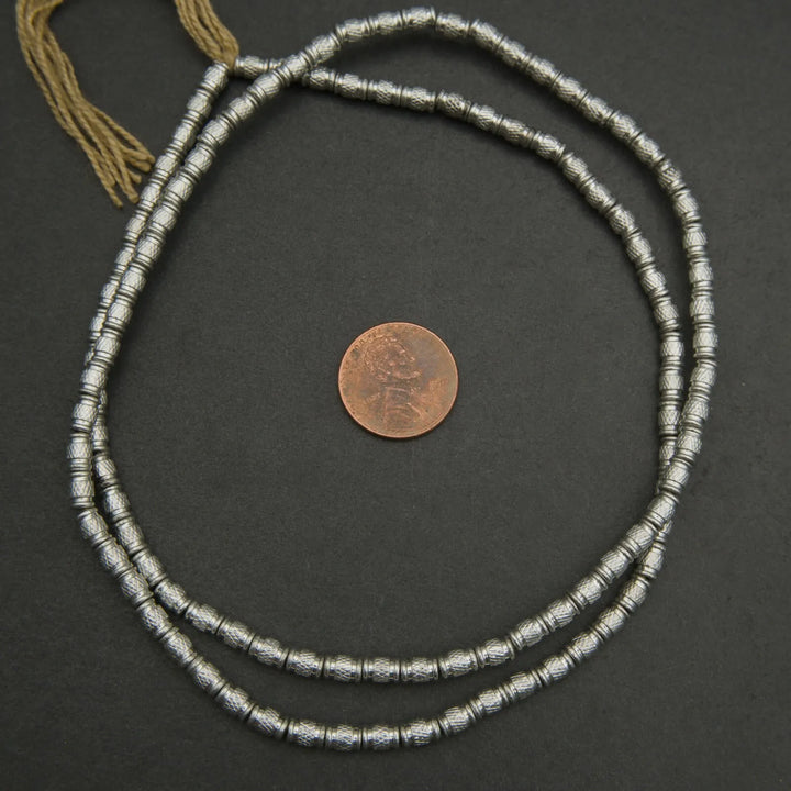 Silver beaded necklace with a coin for scale on a dark surface