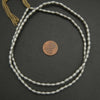 Silver beaded necklace with a coin for scale on a dark surface