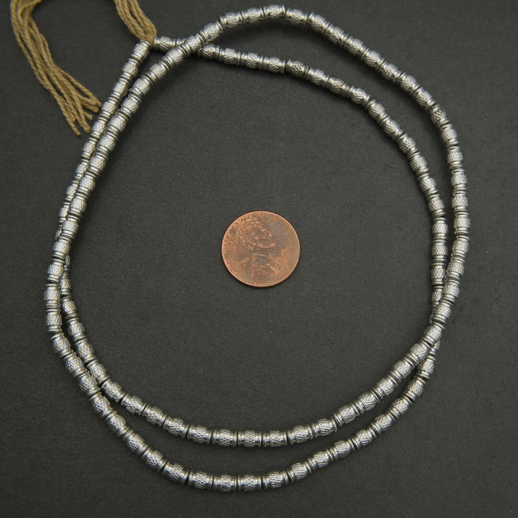 Silver beaded necklace with a coin for scale on a dark surface