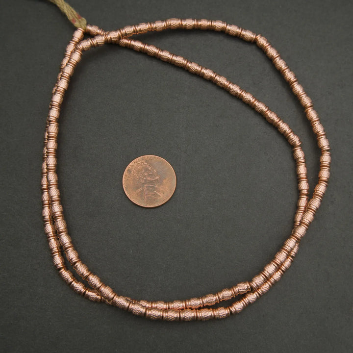 Copper beaded necklace with a coin for scale on a dark background