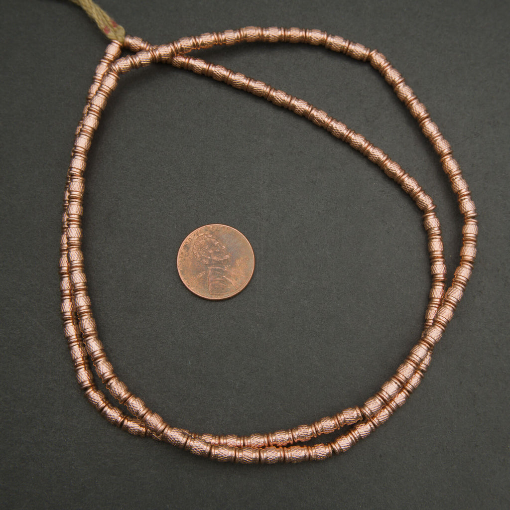 Copper beaded necklace with a coin for scale on a dark background