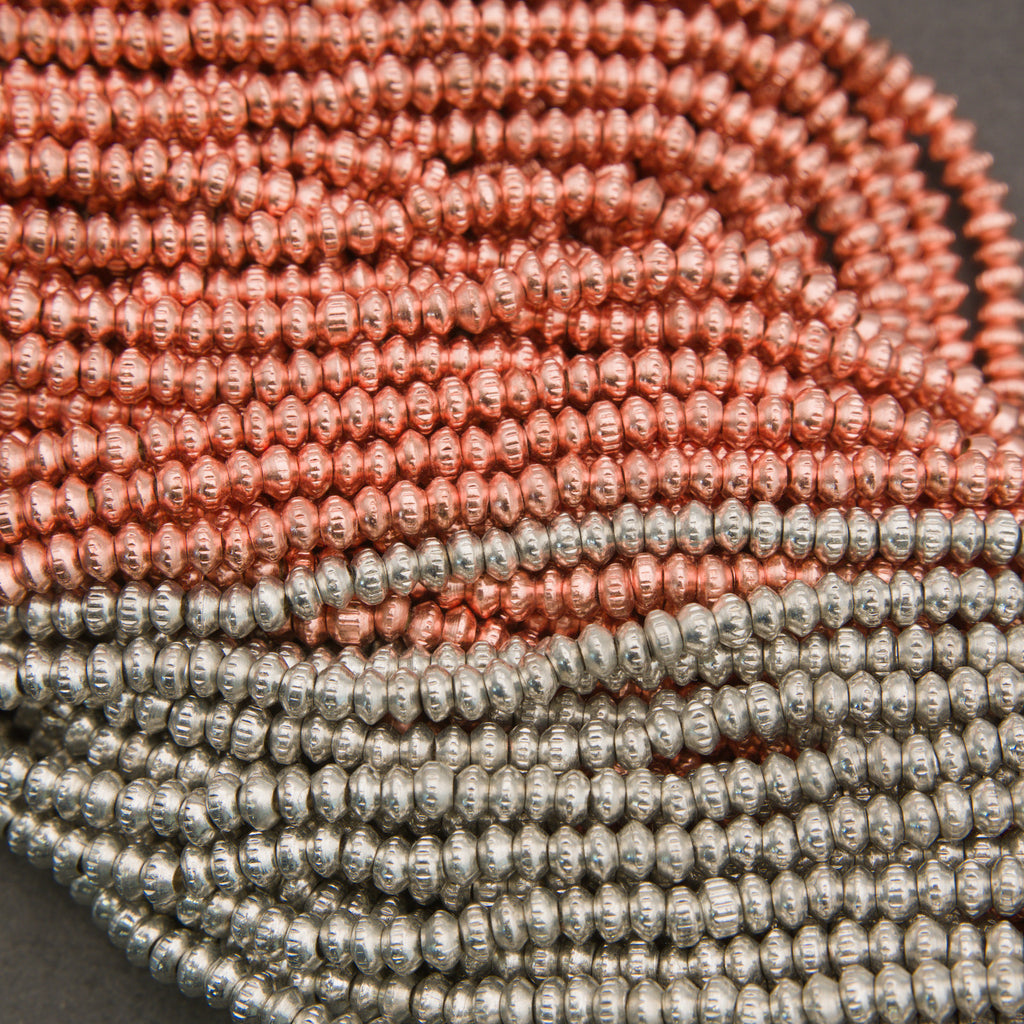 Close-up of two strands of beads, one pink and one silver, on a dark background.