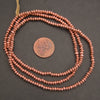 Copper beaded necklace with a penny for scale on a dark background