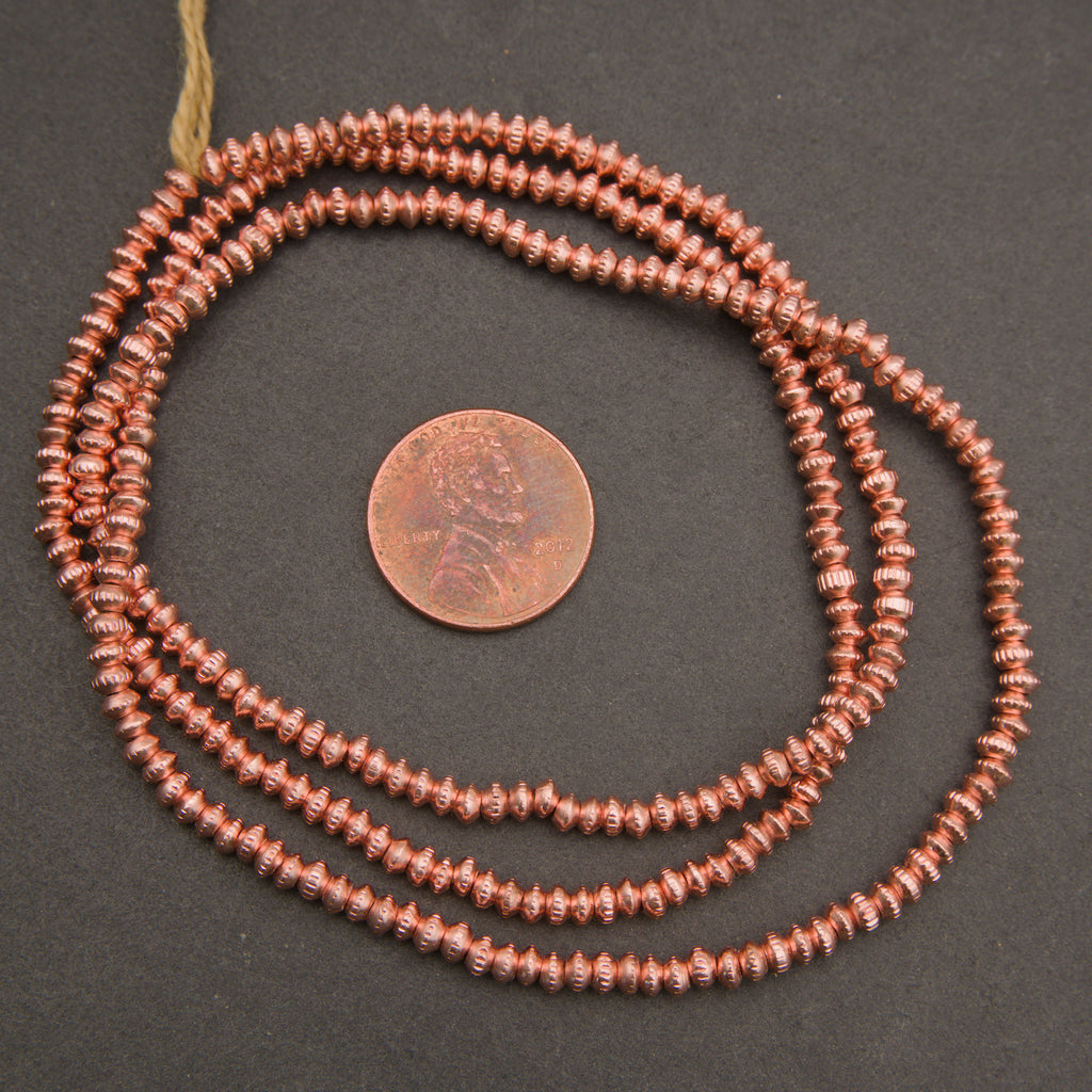 Copper beaded necklace with a penny for scale on a dark background