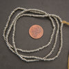 Silver beaded necklace with a penny for scale on a dark surface