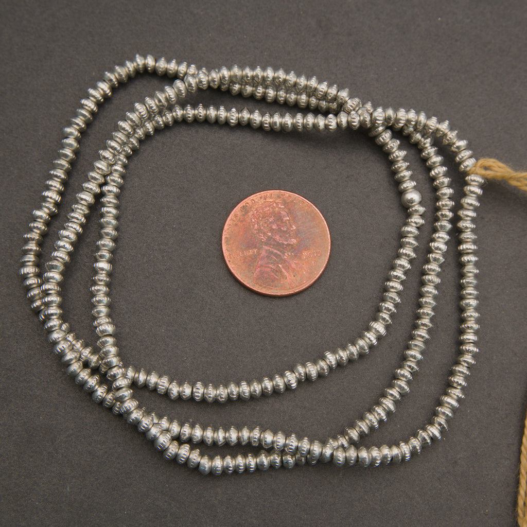 Silver beaded necklace with a penny for scale on a dark surface