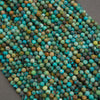 A close-up pile of faceted round beads in a mottled turquoise, teal, green, blue, and brown colorway, resting on a dark gray surface.
