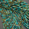 A close-up pile of round turquoise beads with natural mottled patterns in shades of blue, green, and brown, arranged on a neutral gray surface.