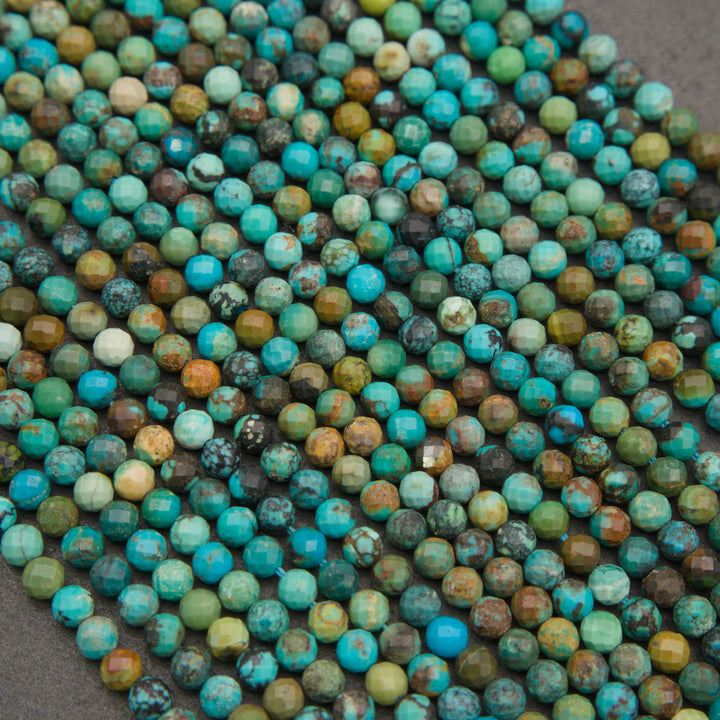A close-up pile of faceted round beads in a mottled turquoise, teal, green, brown, and cream stone pattern, arranged on a dark gray surface.