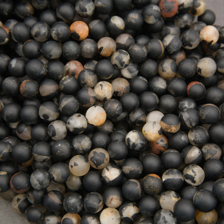 Multiple strands of matte calico tourmaline round beads displaying unique black, white, beige, and orange color variations.