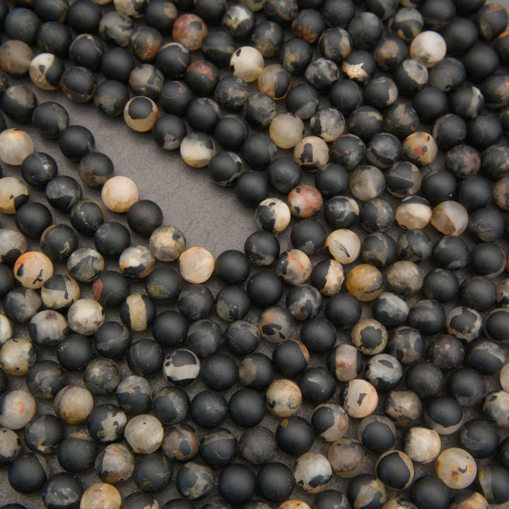 Strands of matte calico tourmaline beads showcasing natural variations in black, gray, ivory, and warm rust tones.