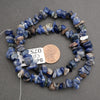 Necklace of blue stone beads with a penny for scale on a gray background