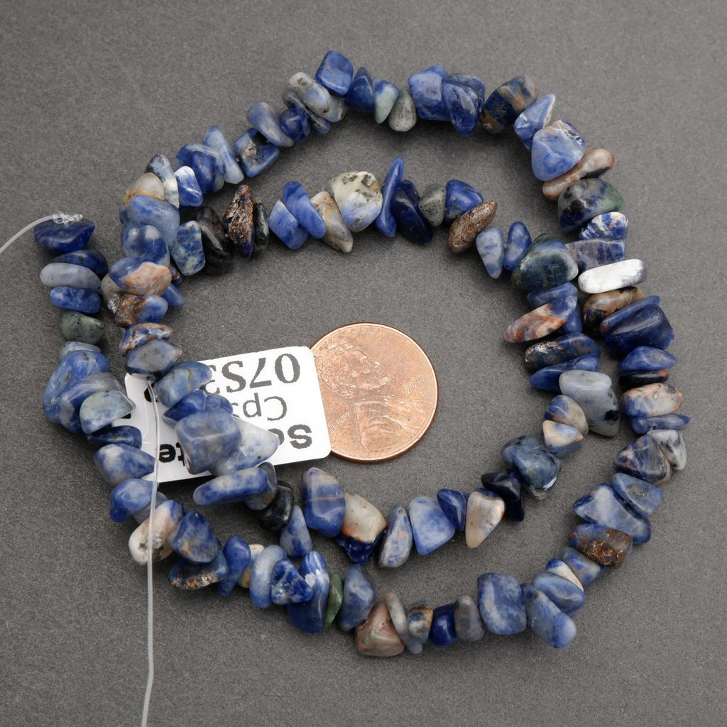 Necklace of blue stone beads with a penny for scale on a gray background