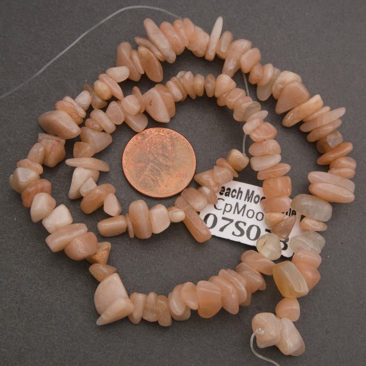 Necklace of peach-colored stone beads with a penny for scale on a gray background