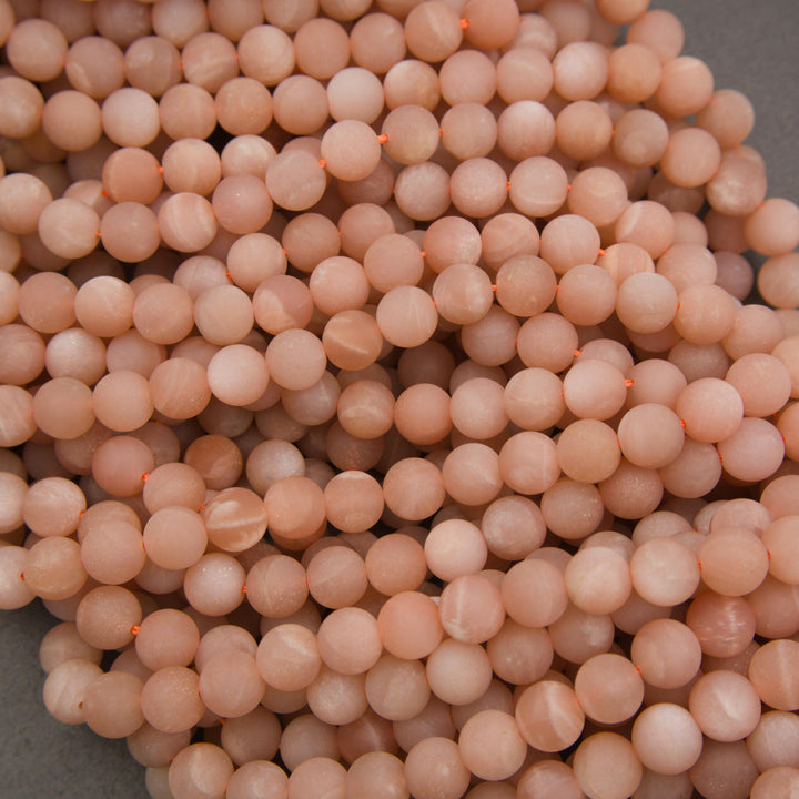Multiple strands of matte peach moonstone round beads displaying warm blush pink and creamy peach color variations.