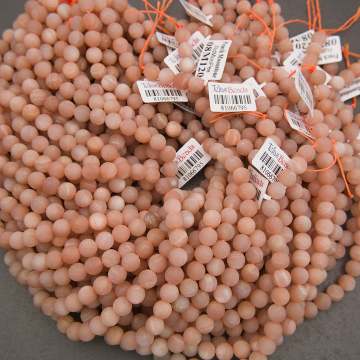 Natural peach moonstone beads featuring soft pastel colors, delicate white banding, and a smooth matte surface.