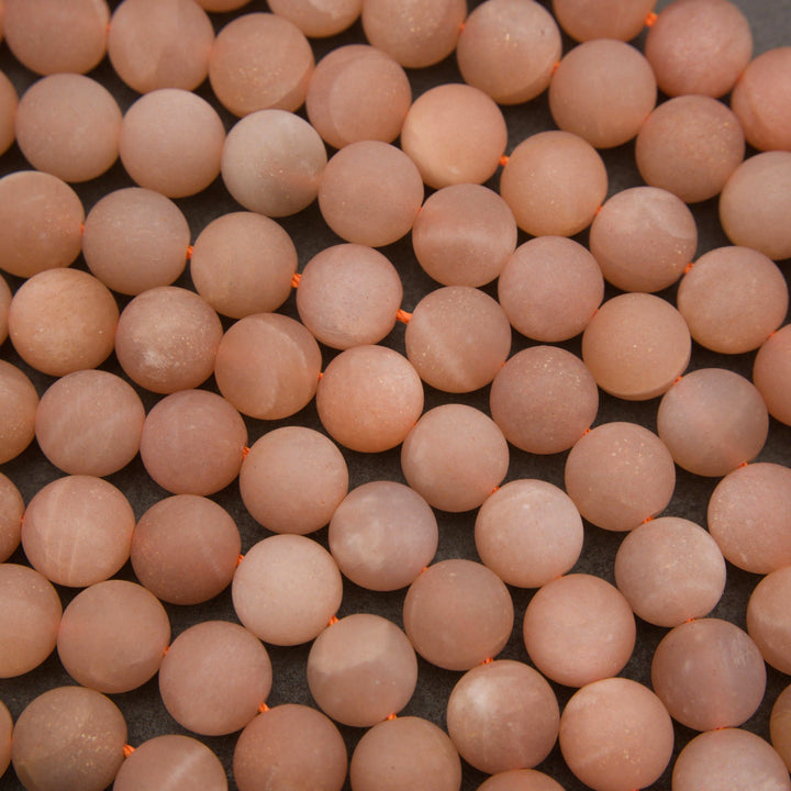 Strands of matte peach moonstone beads showcasing natural variations in peach, blush pink, and creamy ivory tones.