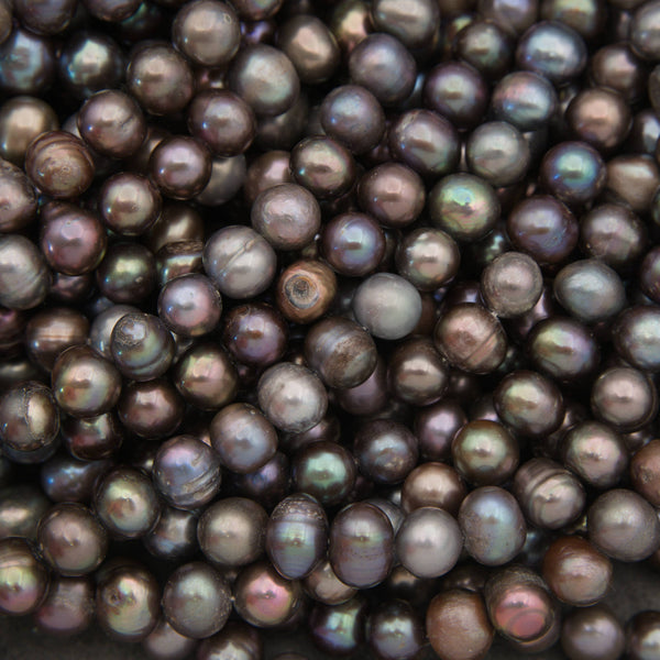 A close-up pile of small round freshwater pearls with a dark, iridescent finish showing shades of brown, gray, and purple.