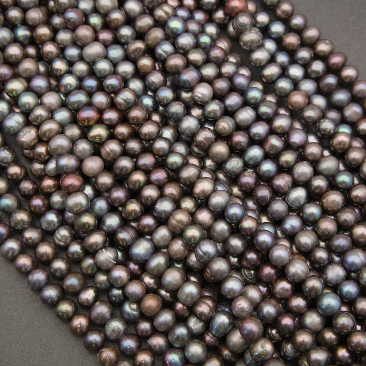 A close-up pile of small round freshwater pearl beads with an iridescent finish, showing shades of dark purple, gray, and green.