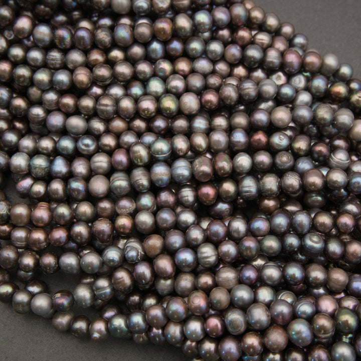 A pile of small, round freshwater pearl beads with a dark, iridescent finish showing hues of purple, green, and blue, set against a dark gray background.