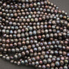 A pile of small, round freshwater pearl beads with a dark, iridescent finish showing hues of purple, green, and blue, set against a dark gray background.