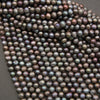 A close-up of a strand of iridescent freshwater pearl beads in a dark gray, bronze, and purple colorway with rainbow reflections, laid out on a dark gray background.
