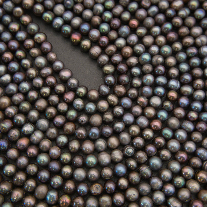 A close-up of many small round iridescent beads or pearls in a dark charcoal-brown tone, arranged to fill the frame with a curved cutout in the center.