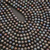 A close-up of many small round iridescent beads or pearls in a dark charcoal-brown tone, arranged to fill the frame with a curved cutout in the center.