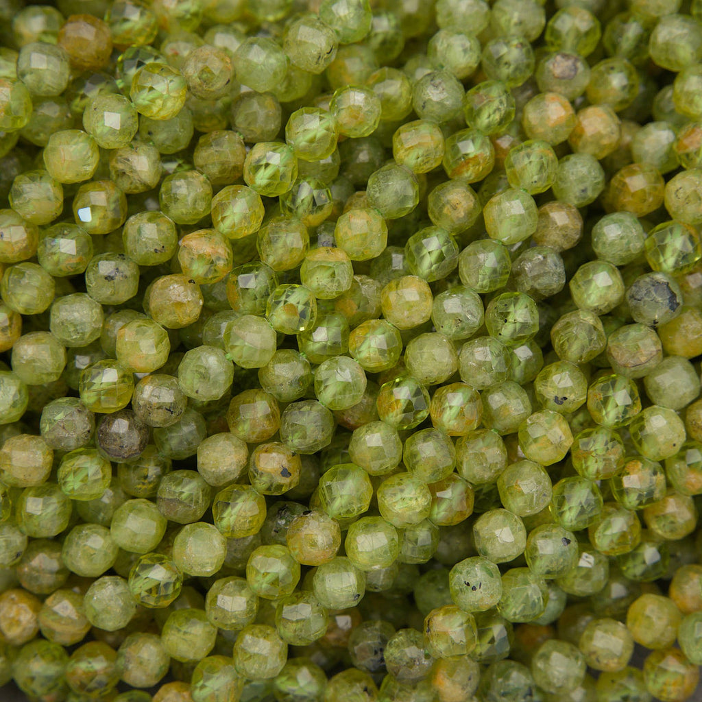 A close-up pile of faceted round beads in a translucent olive green color with natural inclusions visible inside.